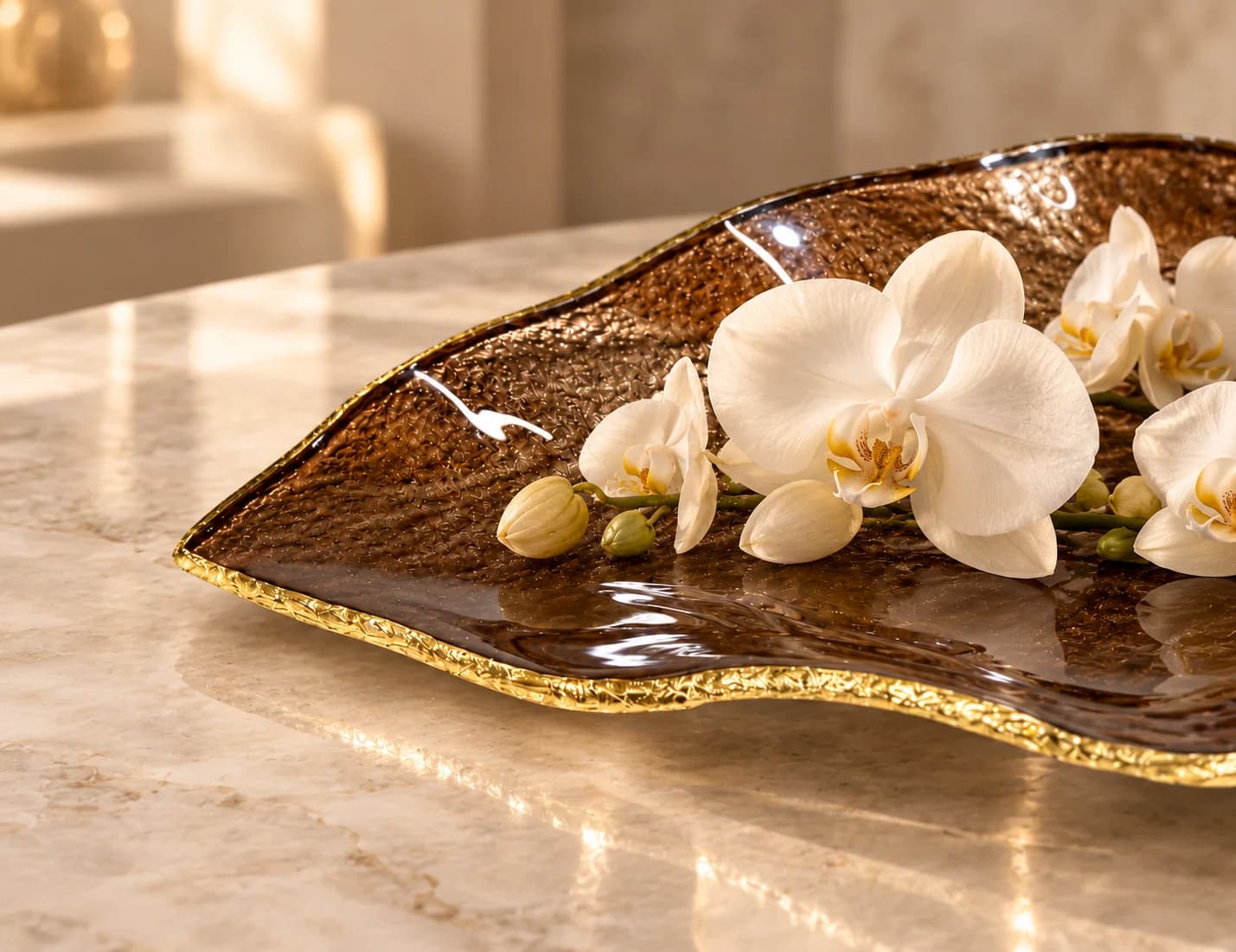 Detalhe de uma peça em vidro marrom com borda dourada e orquídeas brancas
